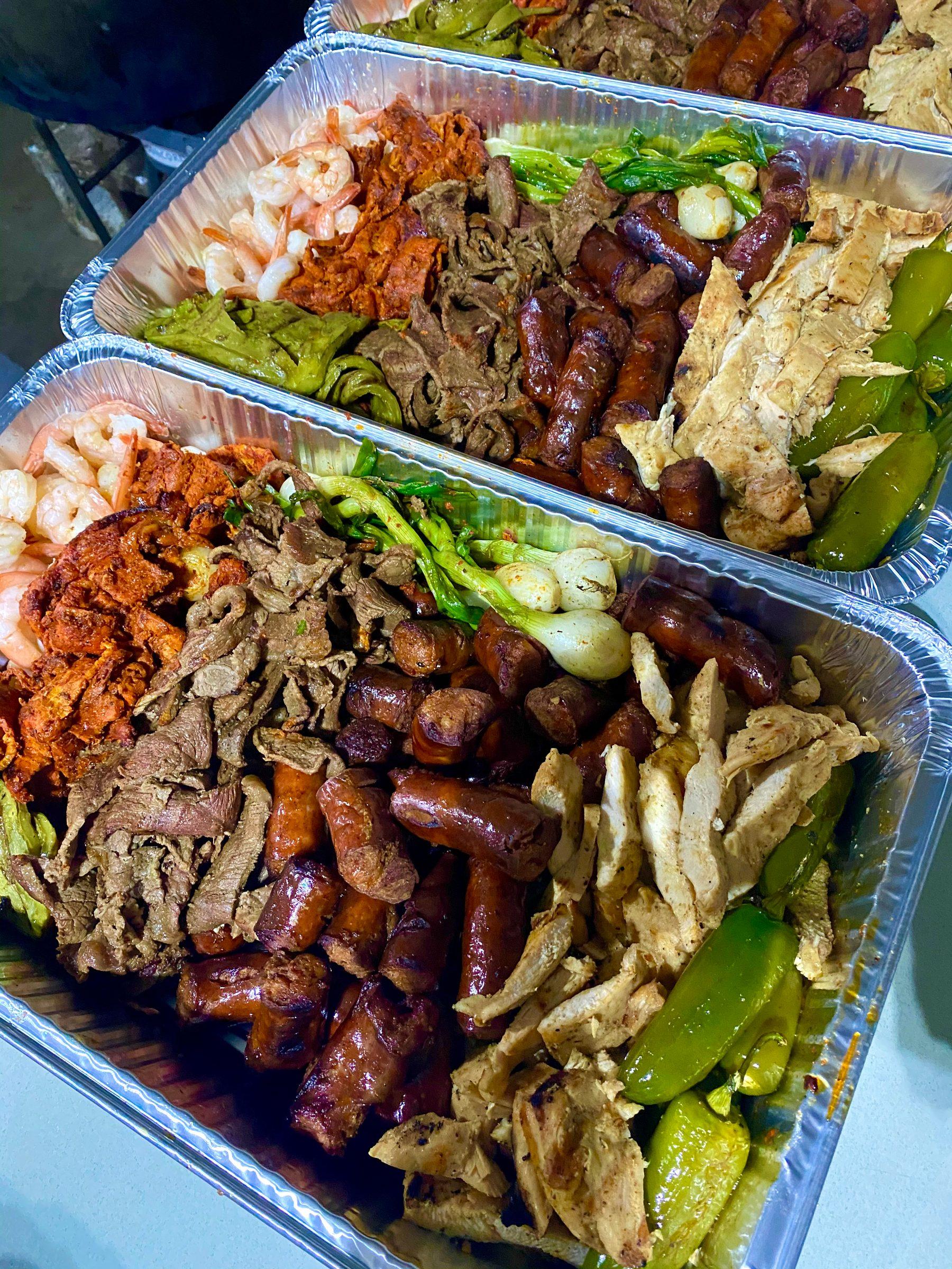 Aluminum family trays of grilled shrimp, al pastor, carne asada, sausages, chicken, cebollitas and chiles toreados