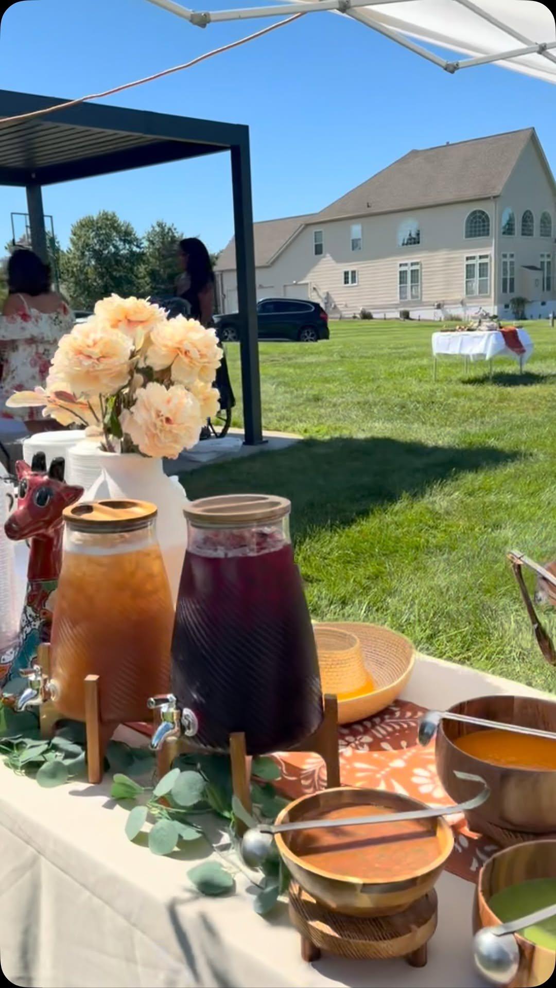 Aguas frescas in glass dispensers beside flowers and salsas at an outdoor engagement party