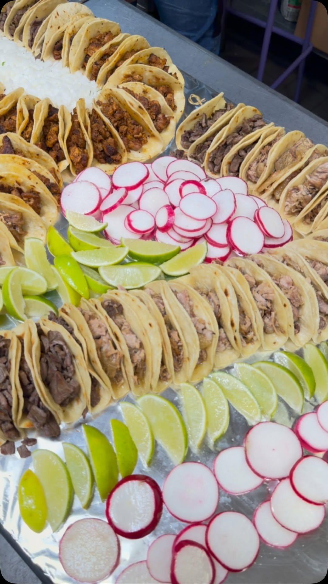 A catering tray of tacos with sliced radishes and lime wedges