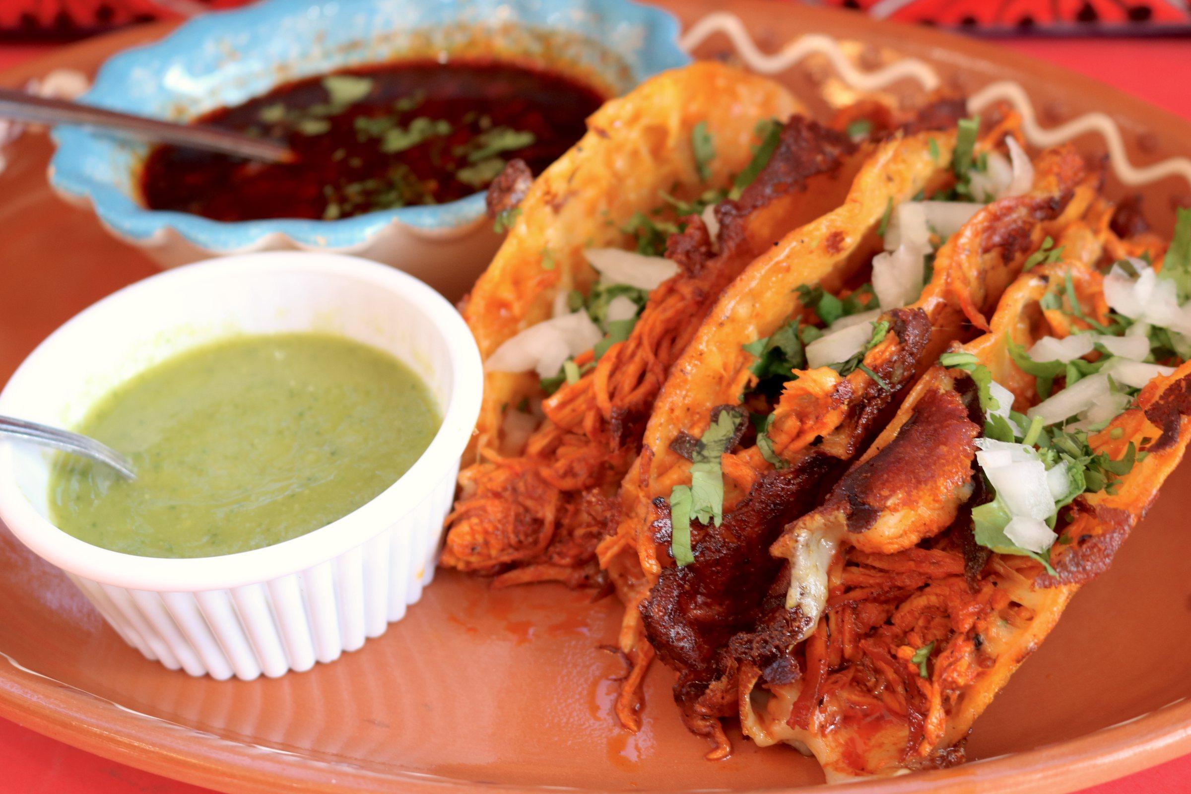 Chicken birria tacos with salsa verde and salsa roja on a terracotta plate