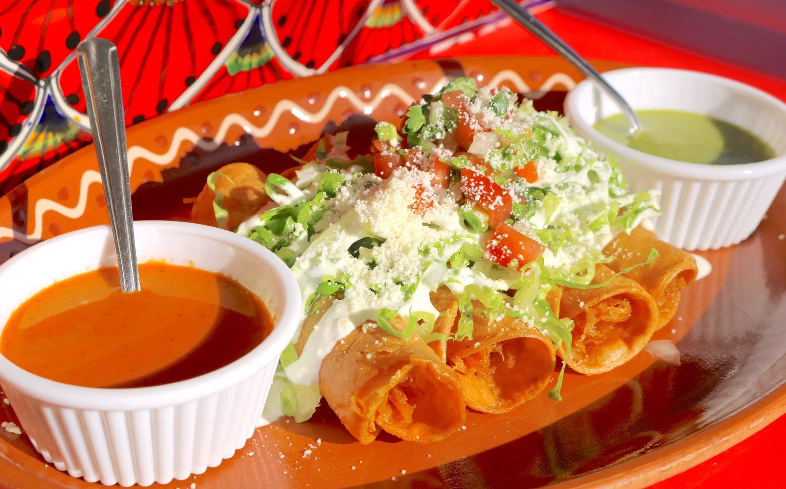 Flautas topped with lettuce, crema and cotija, with salsa roja and salsa verde